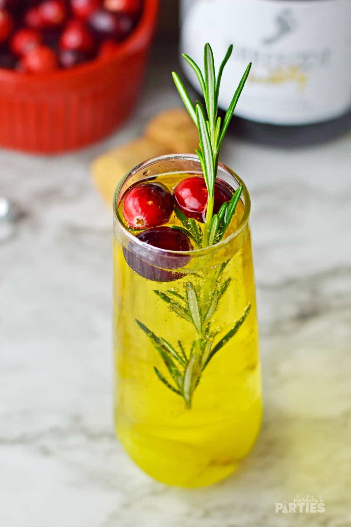 A champagne flute filled with a mimosa mixture, cranberries, and rosemary.