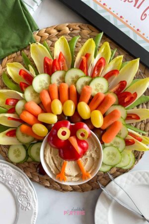 A veggie platter turkey for Thanksgiving with appetizer plates and napkins nearby.