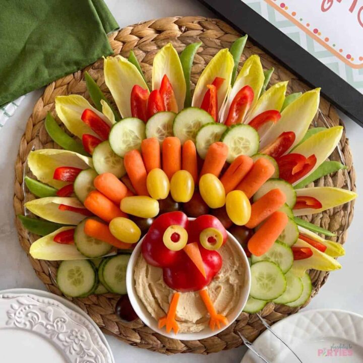 A veggie platter turkey for Thanksgiving with appetizer plates and napkins nearby.