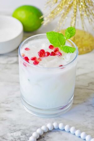 A white Christmas mojito garnished with pomegranate and fresh mint sits on a marble surface.