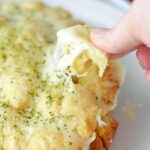 A woman's hand holding a piece of cheesy crock pot pull apart bread.