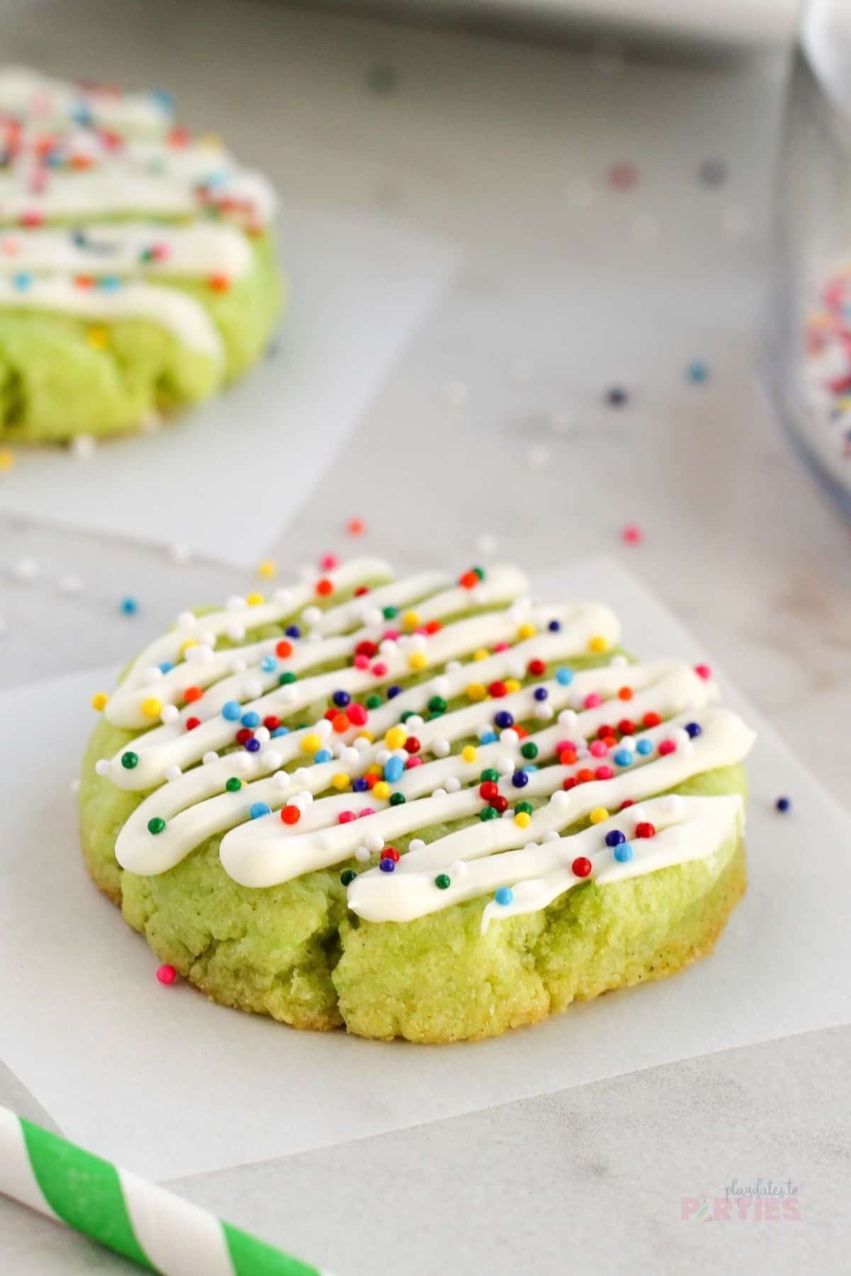 A lime cookie decorated with white chocolate and sprinkles.