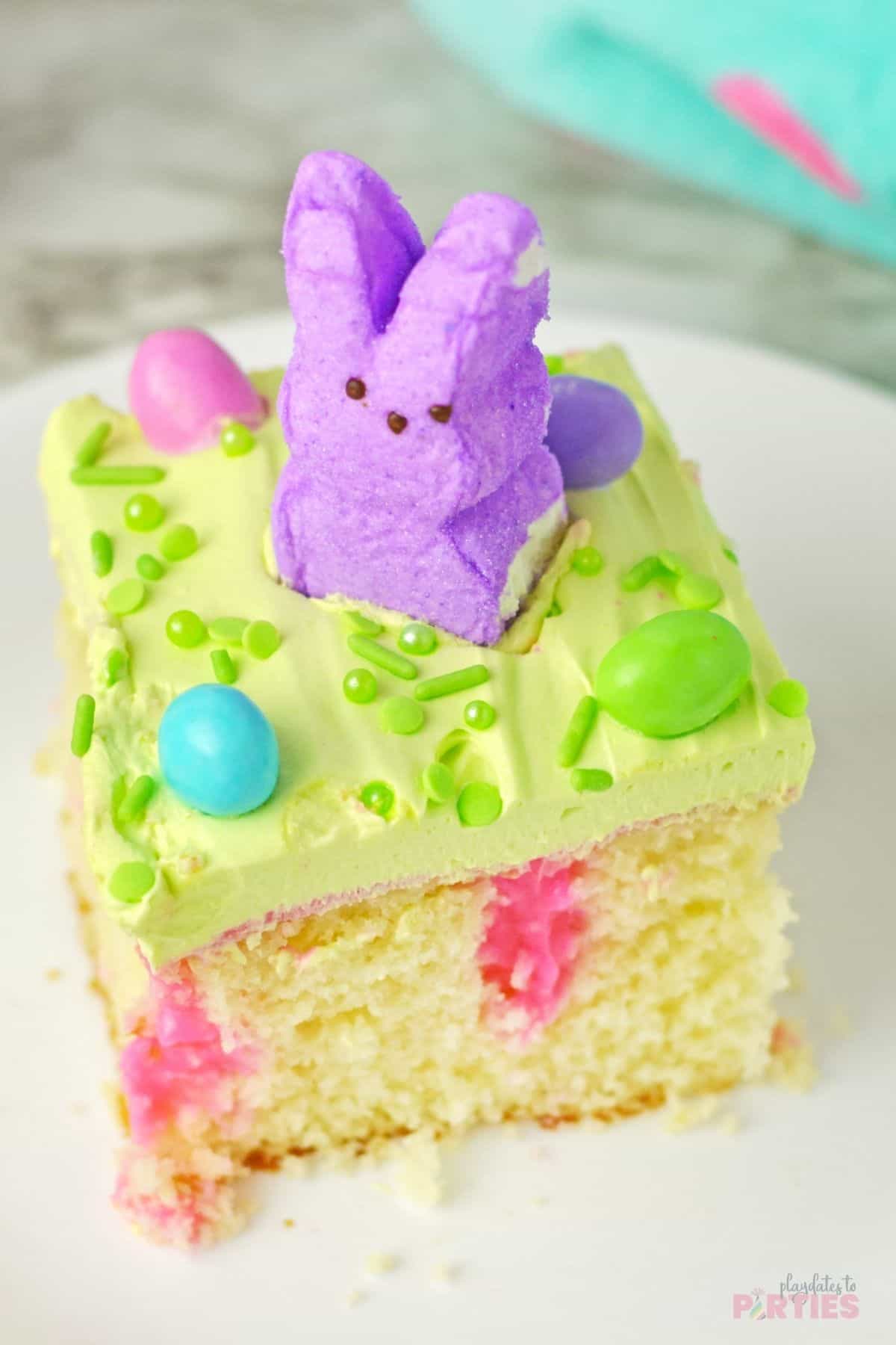 A slice of Easter Peeps poke cake with pink pudding, green frosting, and M&Ms.