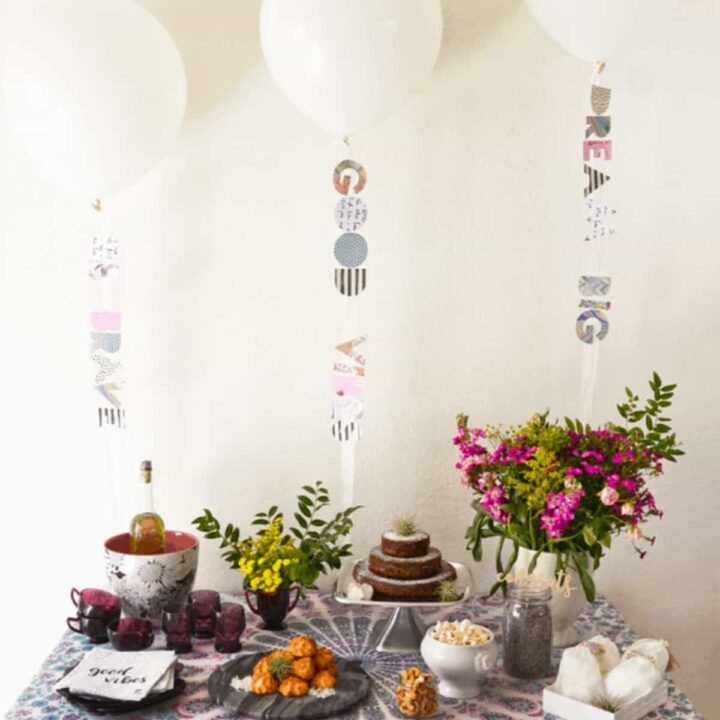 Boho themed baby shower dessert table with white balloons floating above.