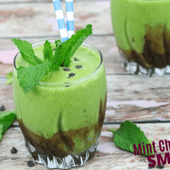 A green mint chocolate chip smoothie garnished with fresh mint on a wood surface.