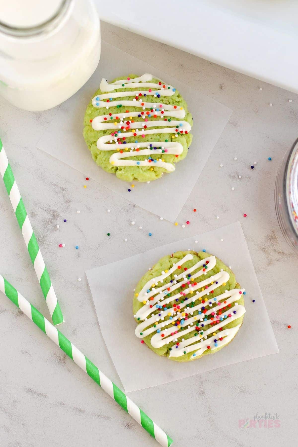 Overhead view of two cookies near a jug of milk and green striped paper straws.