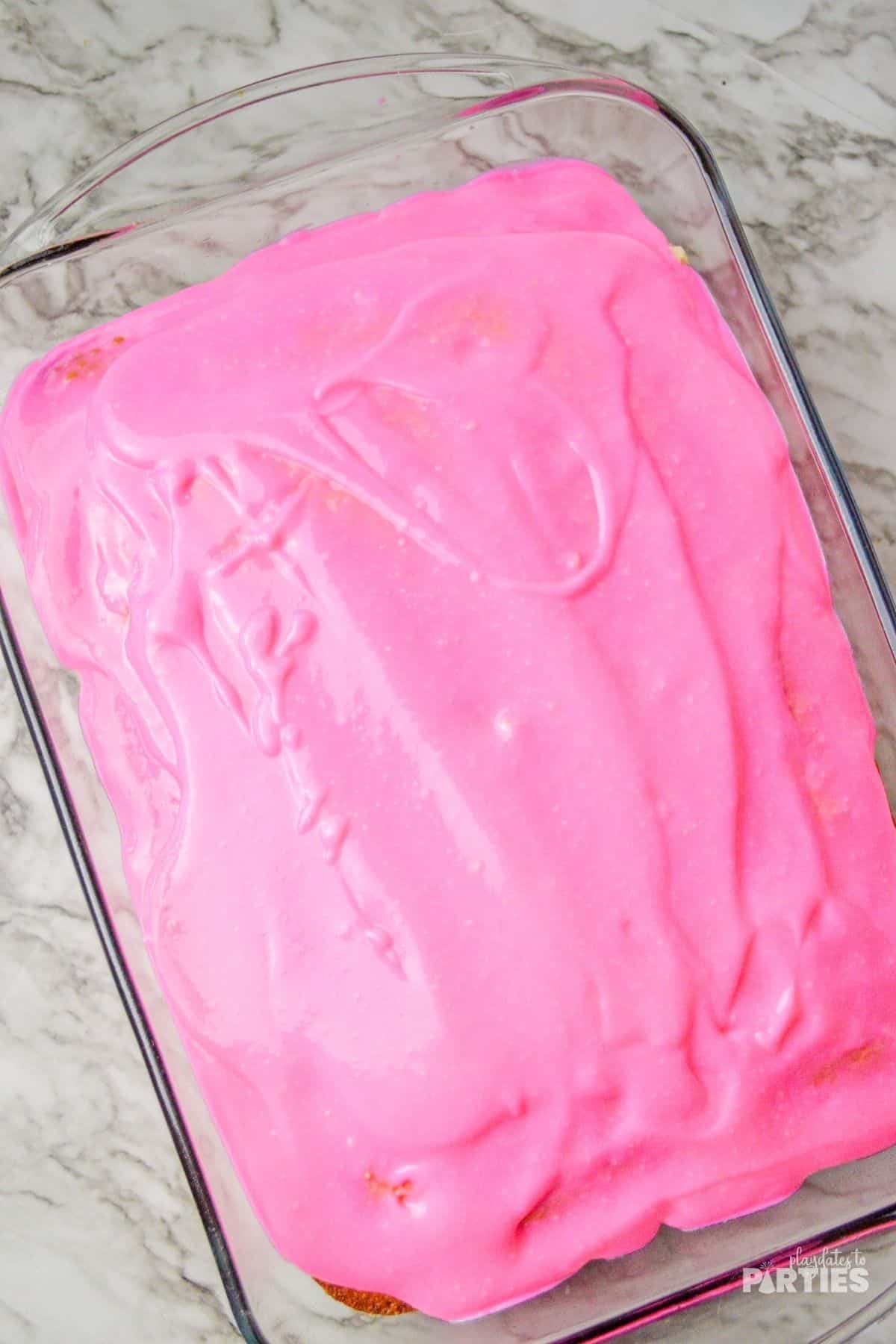 Pouring pink pudding mix over the poke cake.