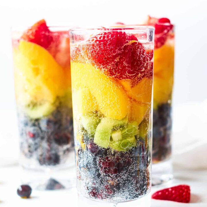 A tall glass filled with a rainbow of fresh fruit for a healthy drink.