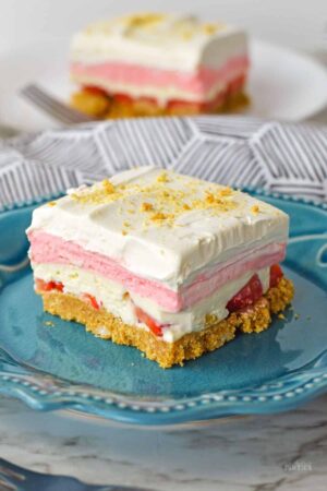 A slice of layered no bake strawberry delight on a blue plate.