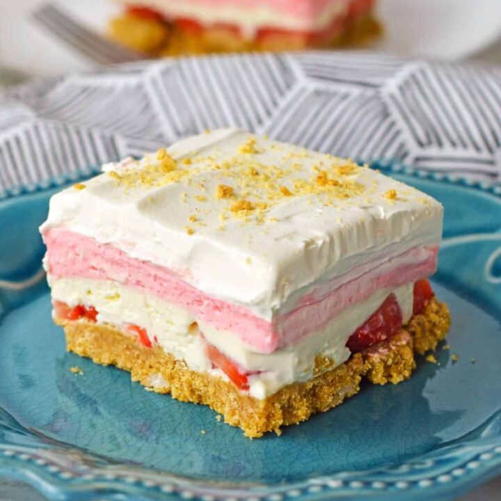 A slice of layered no bake strawberry delight on a blue plate.