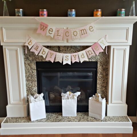 A fireplace mantel decorated with a pink and gold banner for a baby shower.