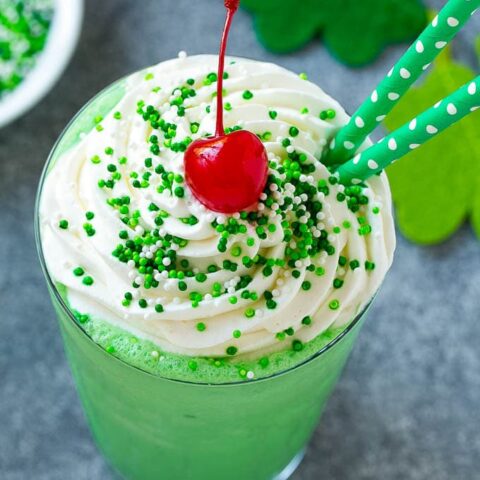 Overhead view of a green shamrock shake for St. Patrick's Day garnished with whipped cream, green sprinkles, and a maraschino cherry.
