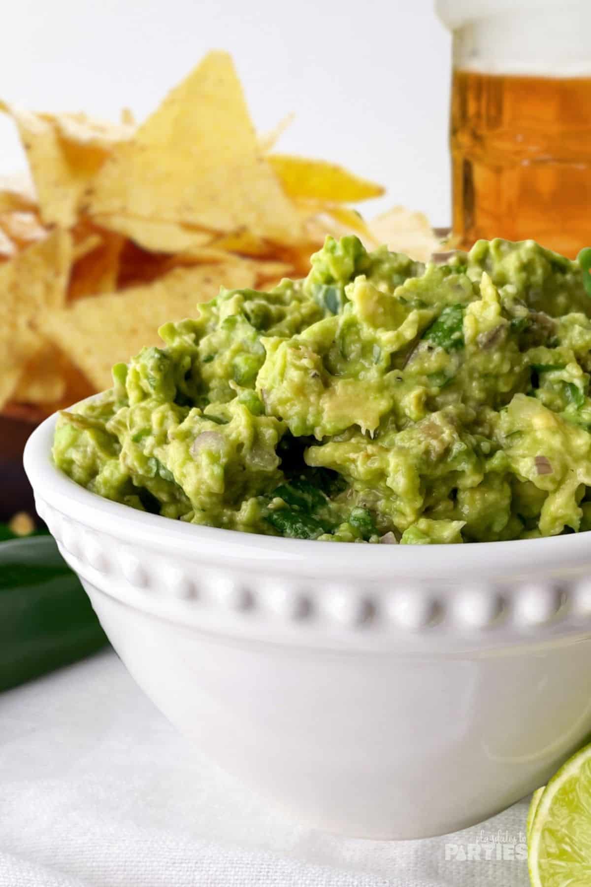 A bowl of avocado dip in front of tortilla chips and a beer
