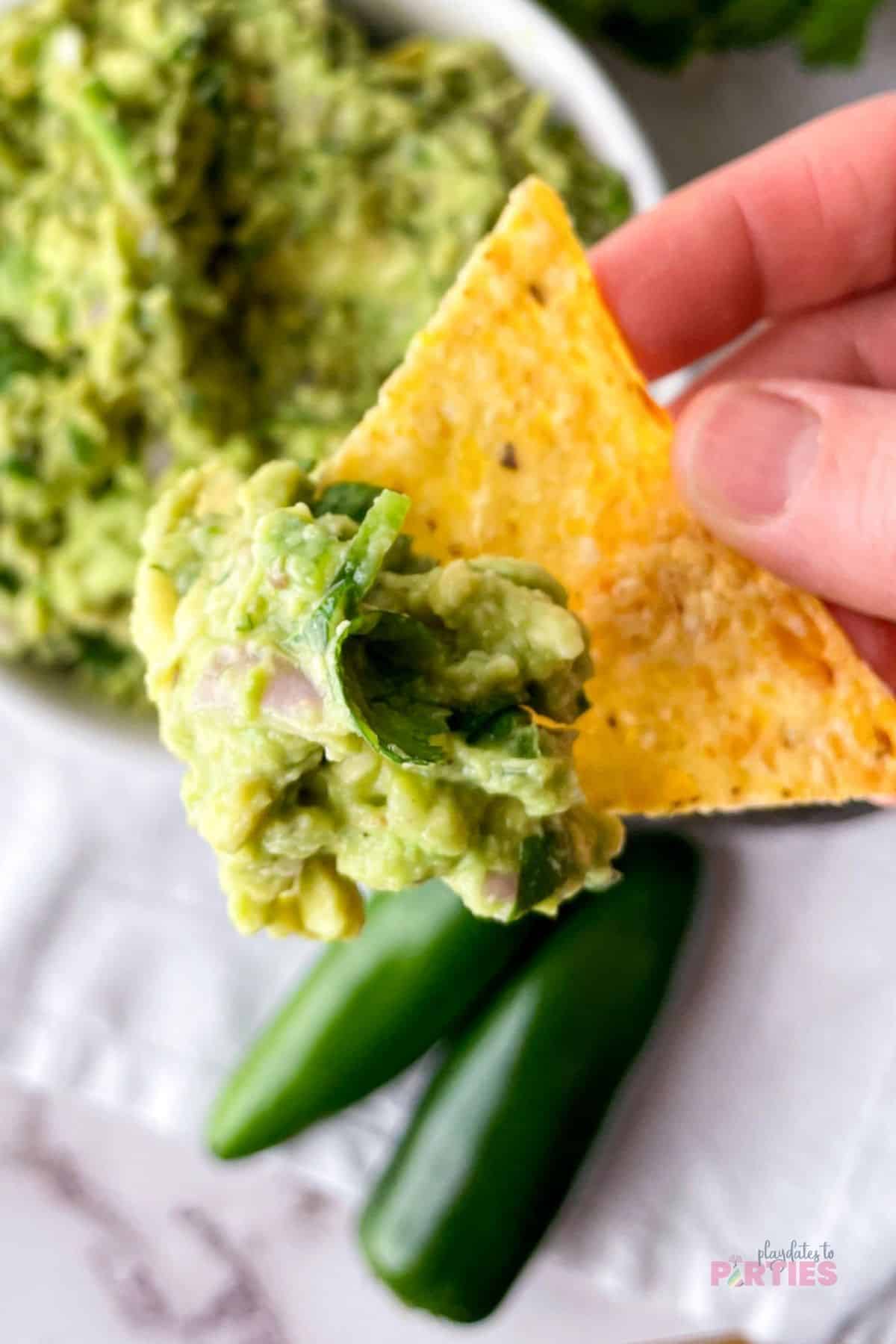 A woman's hand holding a chip with guacamole on it.