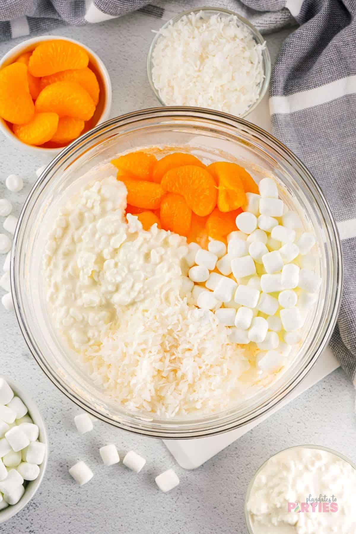 Adding marshmallows, mandarins, cottage cheese and coconut to fluff salad.