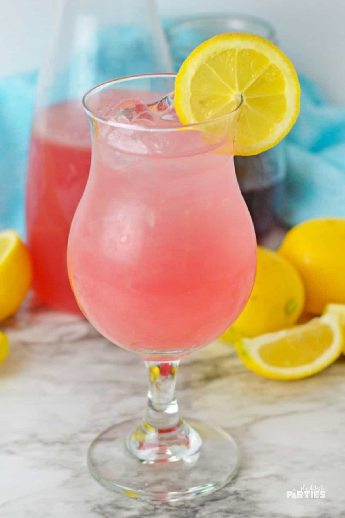 Glass of easy pink lemonade on a marble surface with lemon wedges nearby.