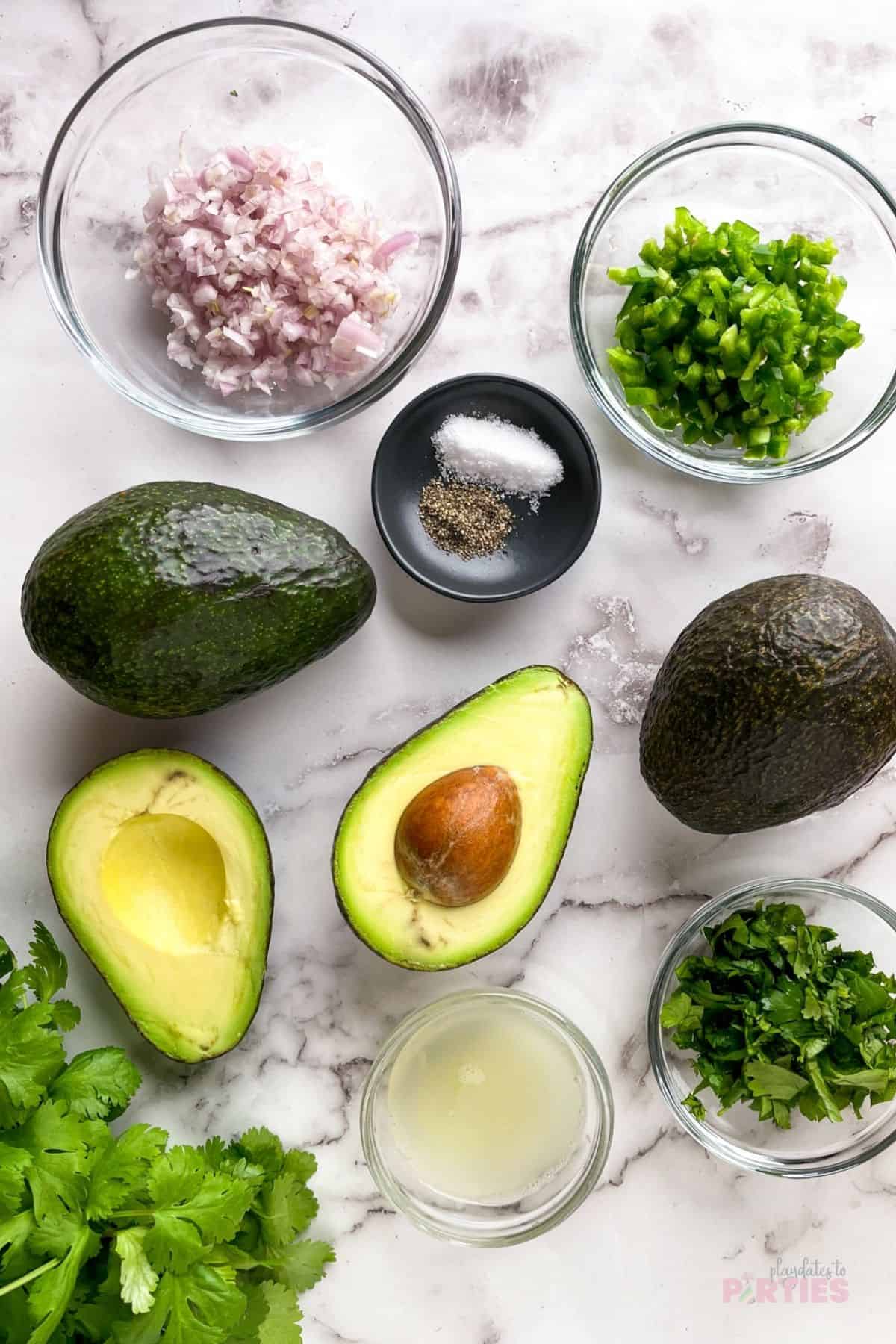 Ingredients on a marble surface include avocado, cilantro, shallot, jalapeno, salt, and pepper.