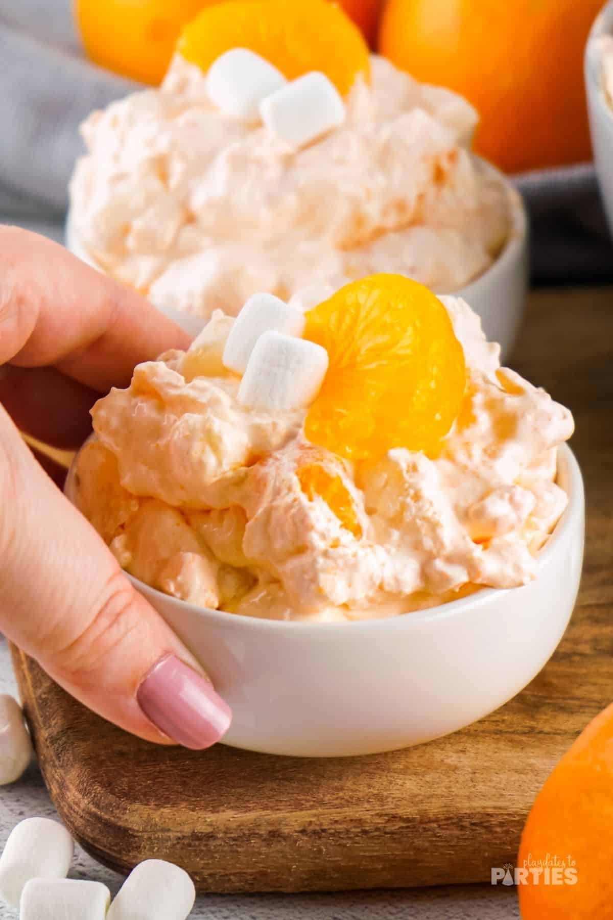 Orange fluff jello salad being picked up by a woman's hand.