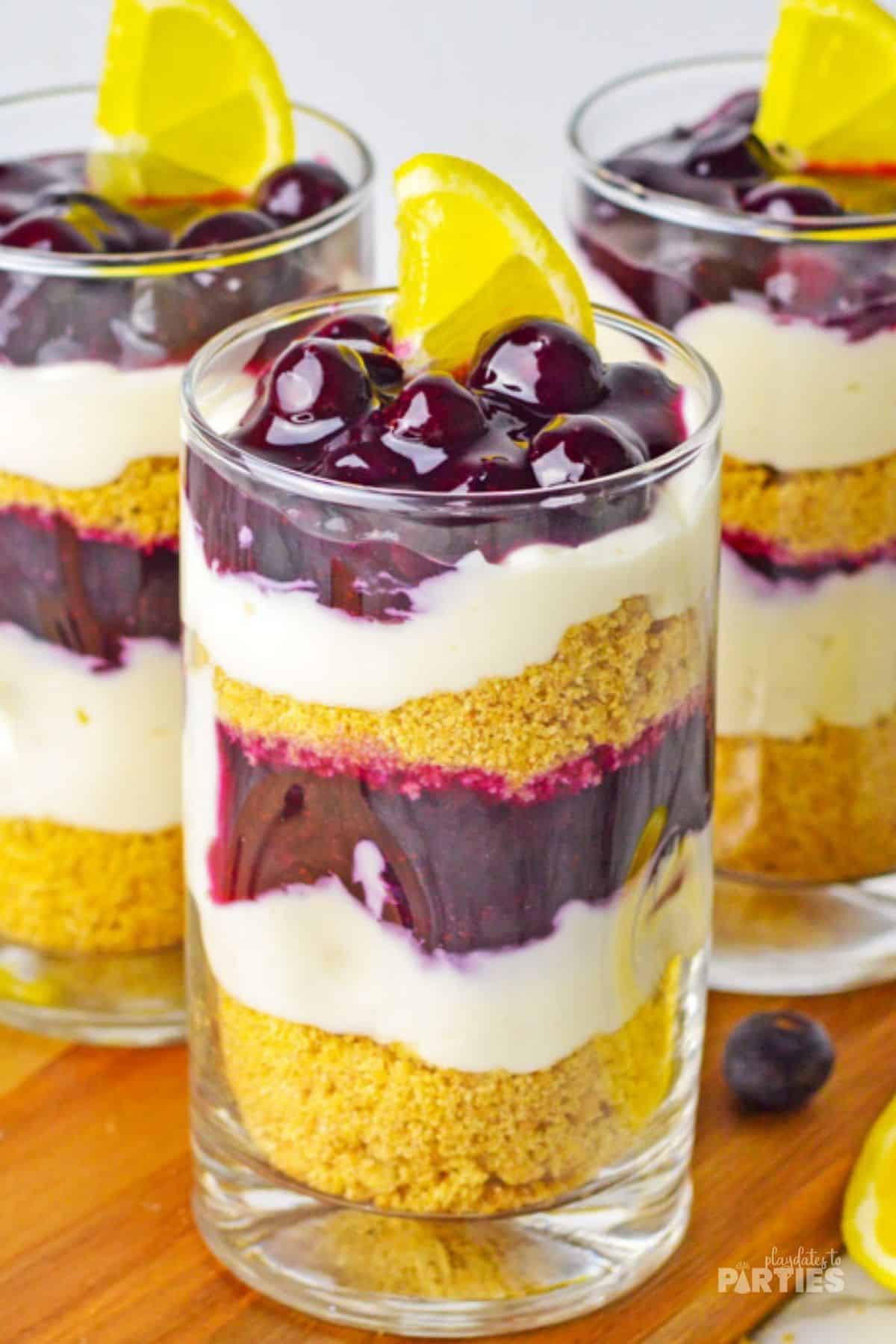 Parfaits made with six layers, including blueberry sauce, cheesecake, and graham crackers.
