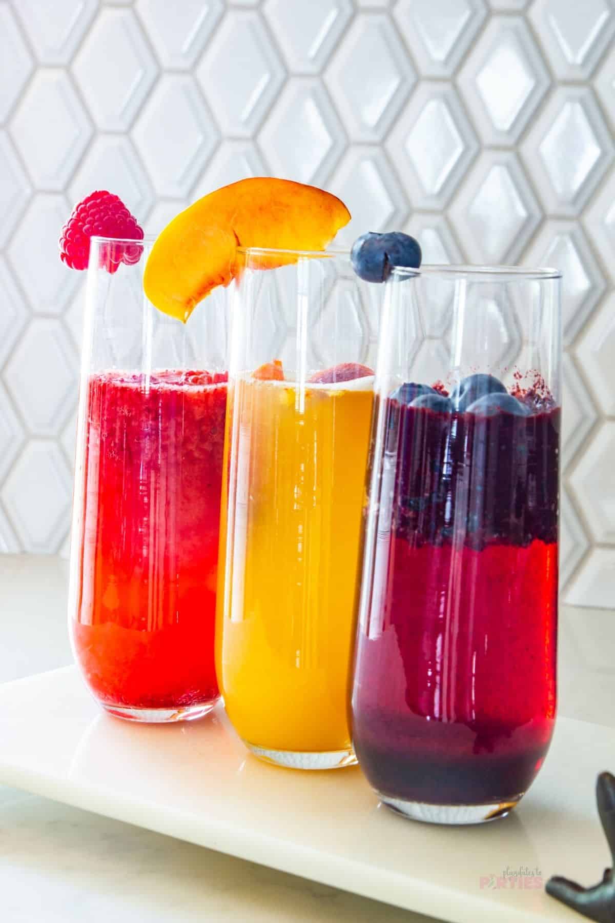 Raspberry, peach, and blueberry bellinis on a white tray.