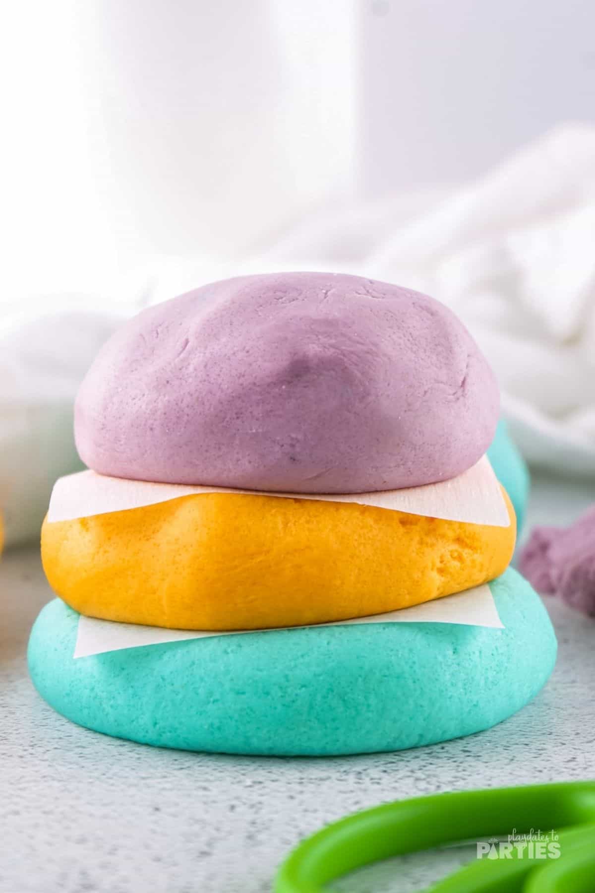 Three colors of homemade playdough stacked with parchment between each layer.