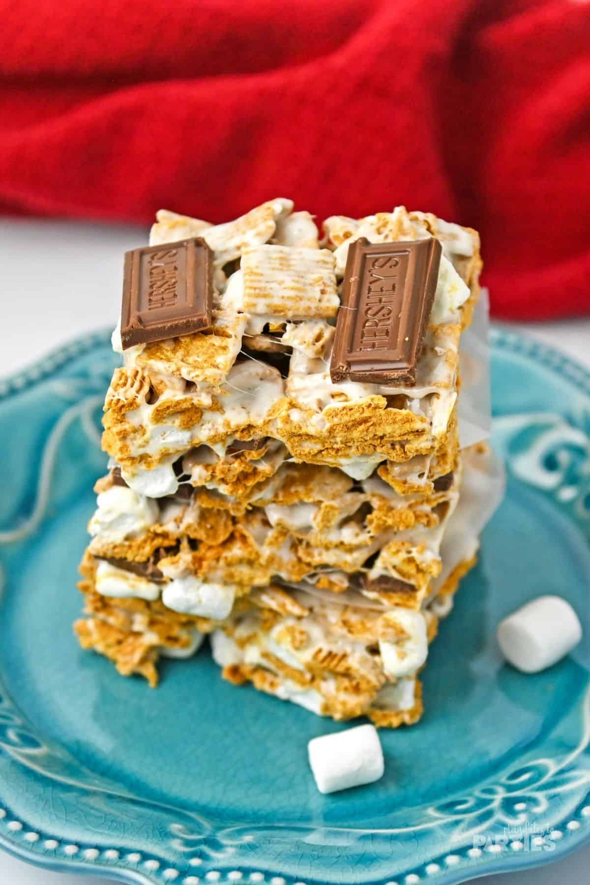 Three S'mores treats are stacked on a blue plate with marshmallows scattered nearby.