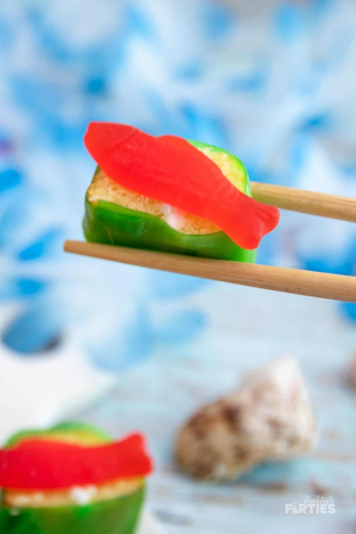 A piece of candy sushi held by chopsticks.