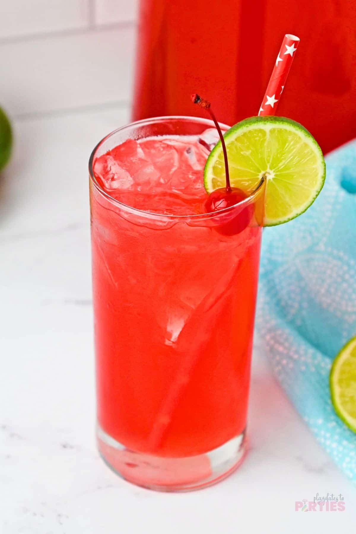 A red drink garnished with a cherry and a lime.
