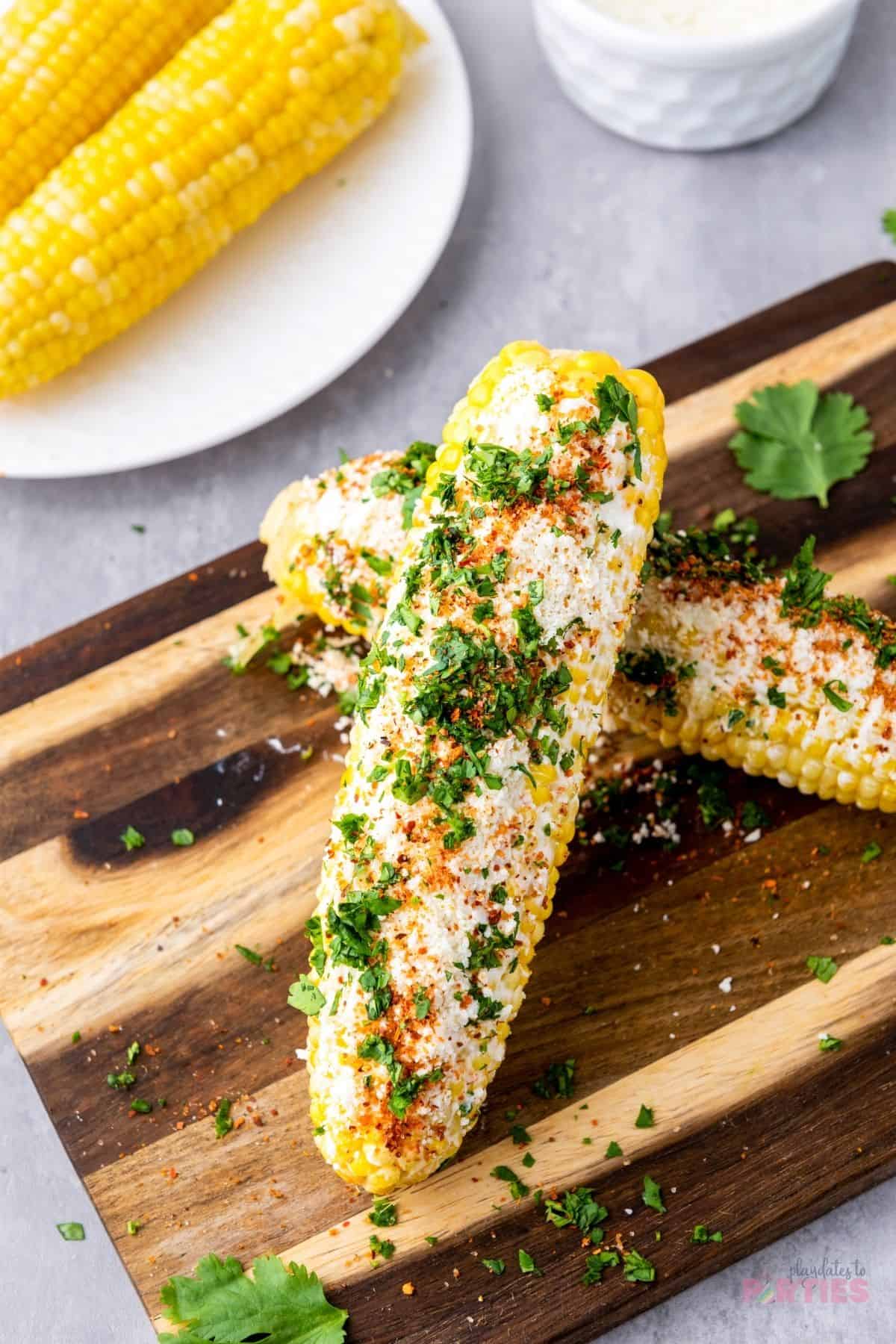 An ear of street corn is smothered with sauce then sprinkled with Cotija cheese, seasonings, and herbs.