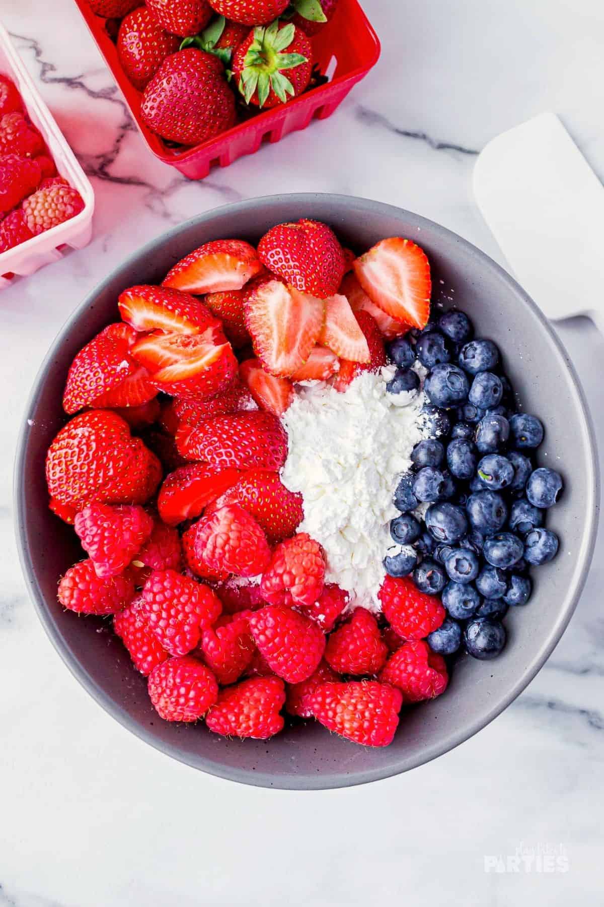 Strawberries, raspberries, and blueberries are mixed in a bowl with cornstarch, juice, and sugar.