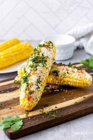 Two mexican elotes corn cobs on a cutting board.
