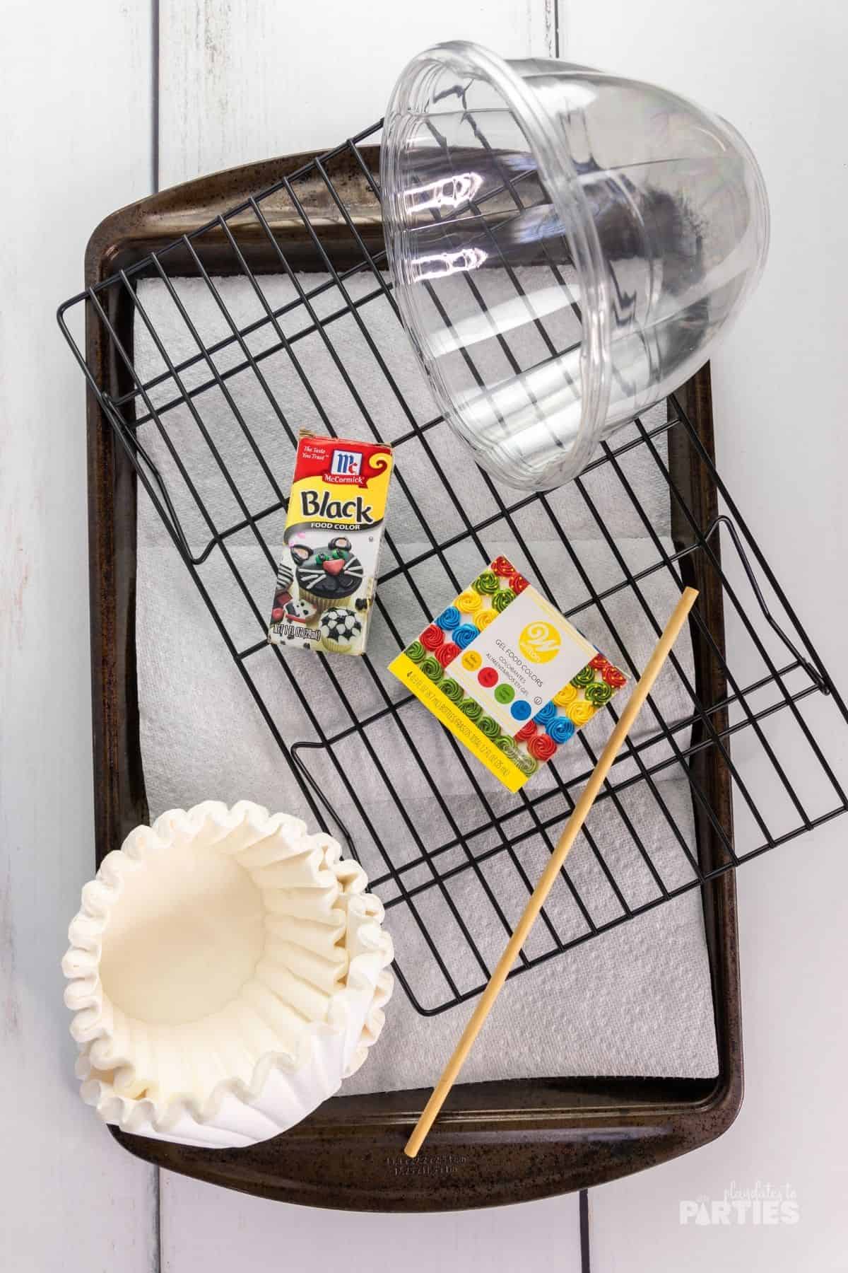 A jellyroll pan with paper towels, coffee filters, food coloring, bowls, a dowel rod, and a drying rack.