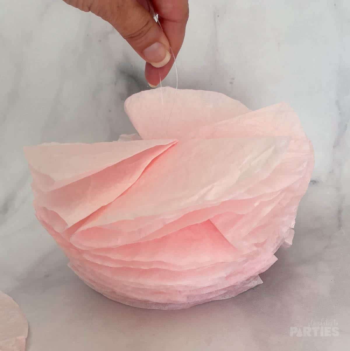 A woman's hand holding the start of a fluffy pink coffee filter garland.