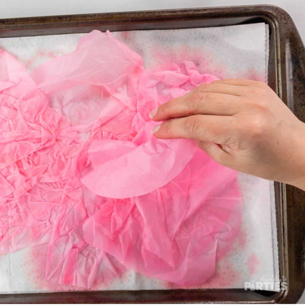 A woman's hand laying pink dyed coffee filters on a paper towel lined cooke sheet.