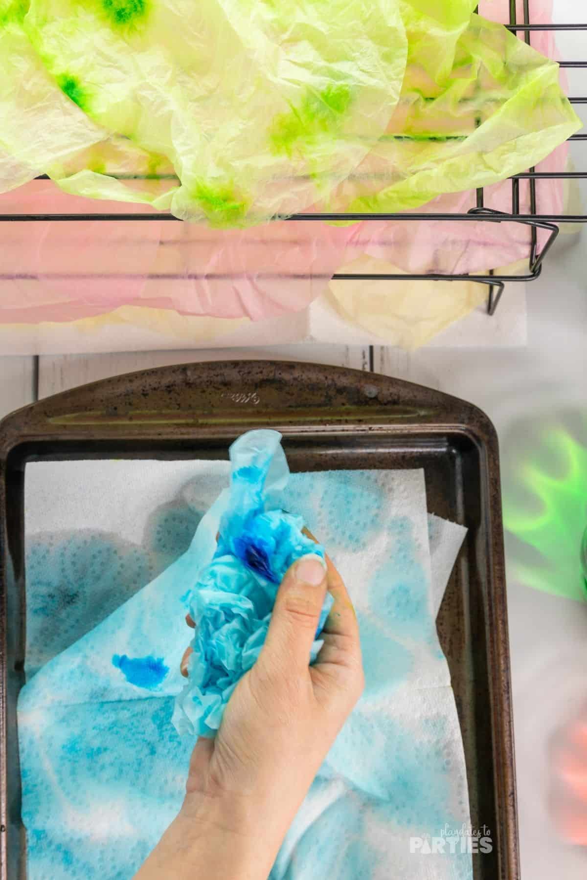 A woman's hand squeezing out excess water from a coffee filter with blue food coloring.
