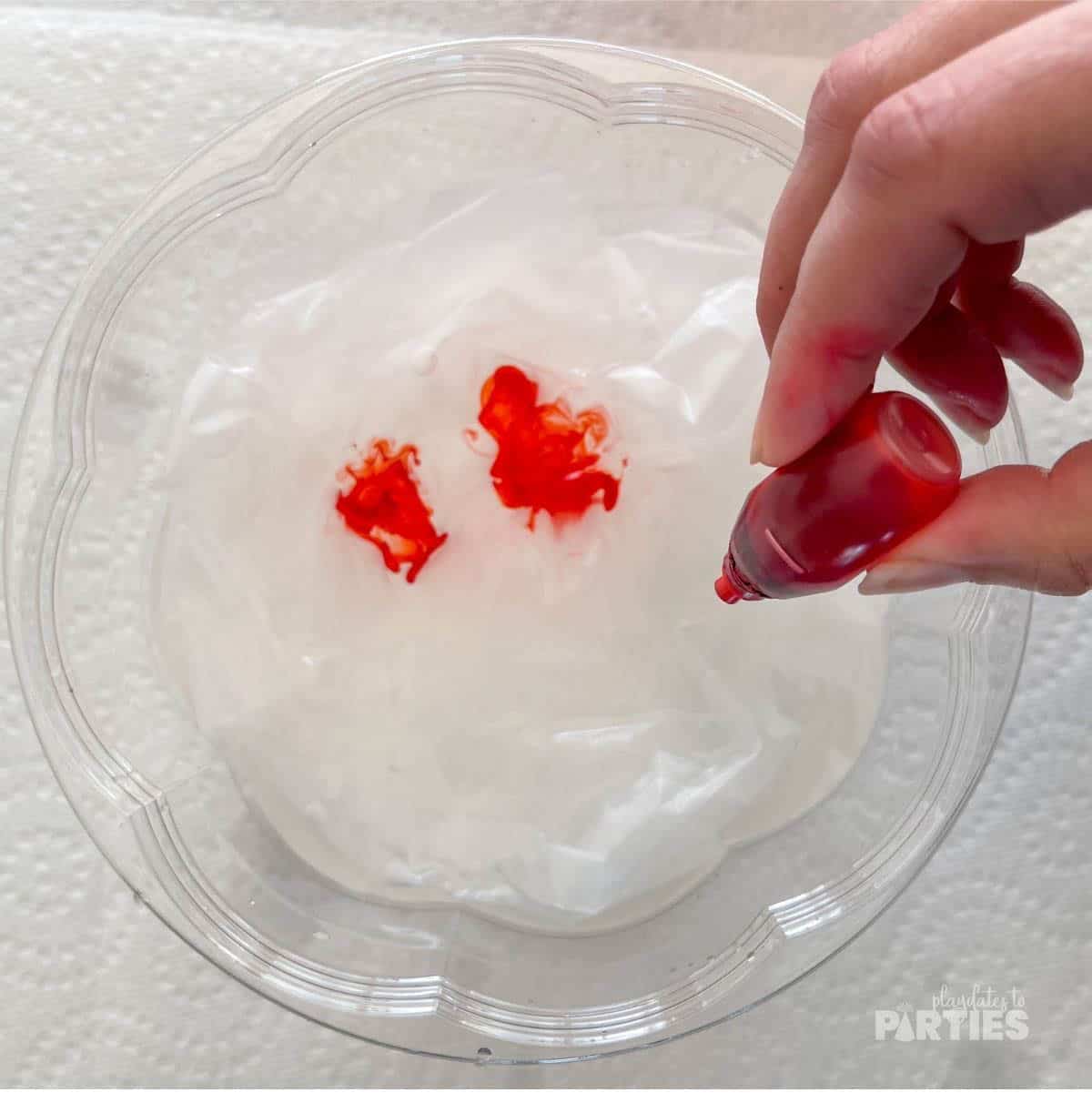 Adding food coloring to a bowl full of water with white coffee filters inside.