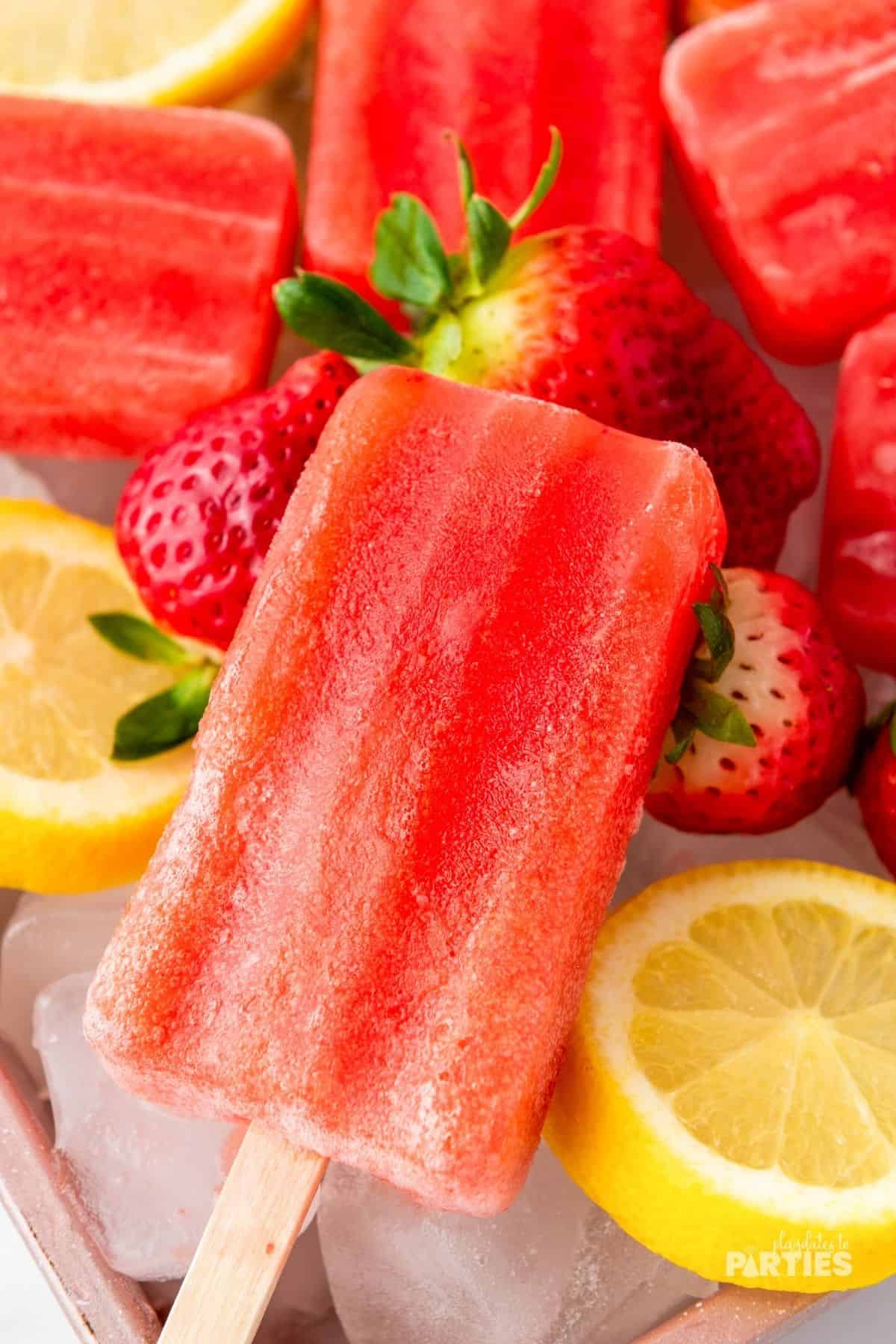 Ice cold strawberry lemonade popsicles are brightly colored and citrusy.