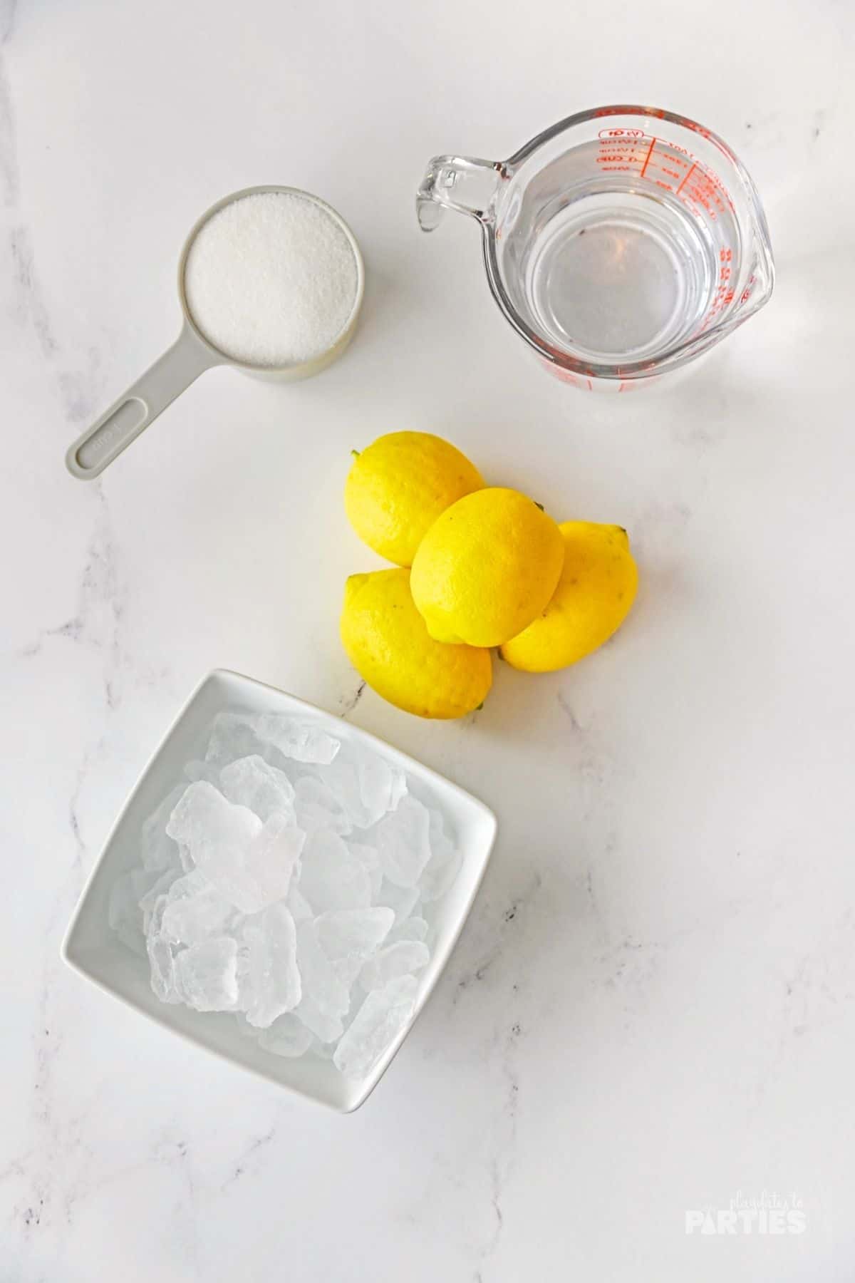 Lemons, water, ice, and sugar on a marble surface.