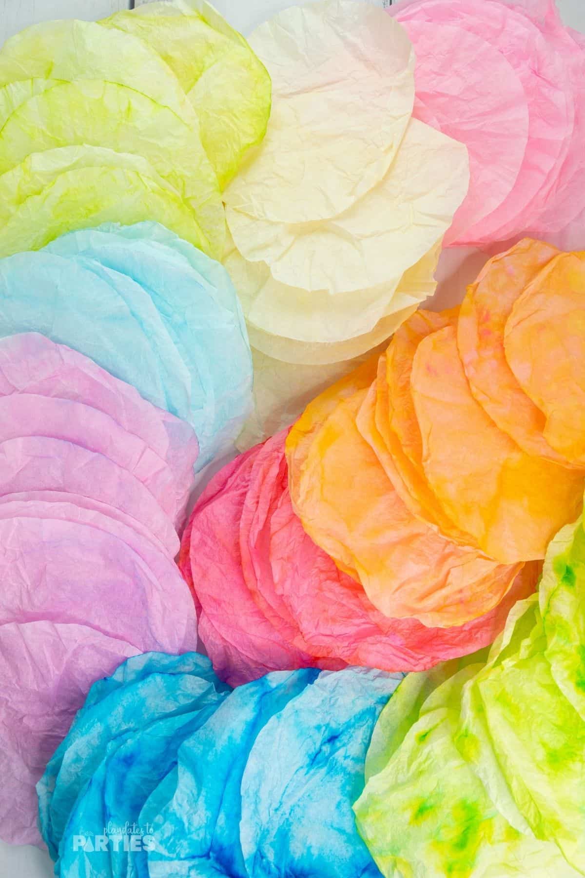 Many colorful dyed coffee filters spread out on a flat surface.
