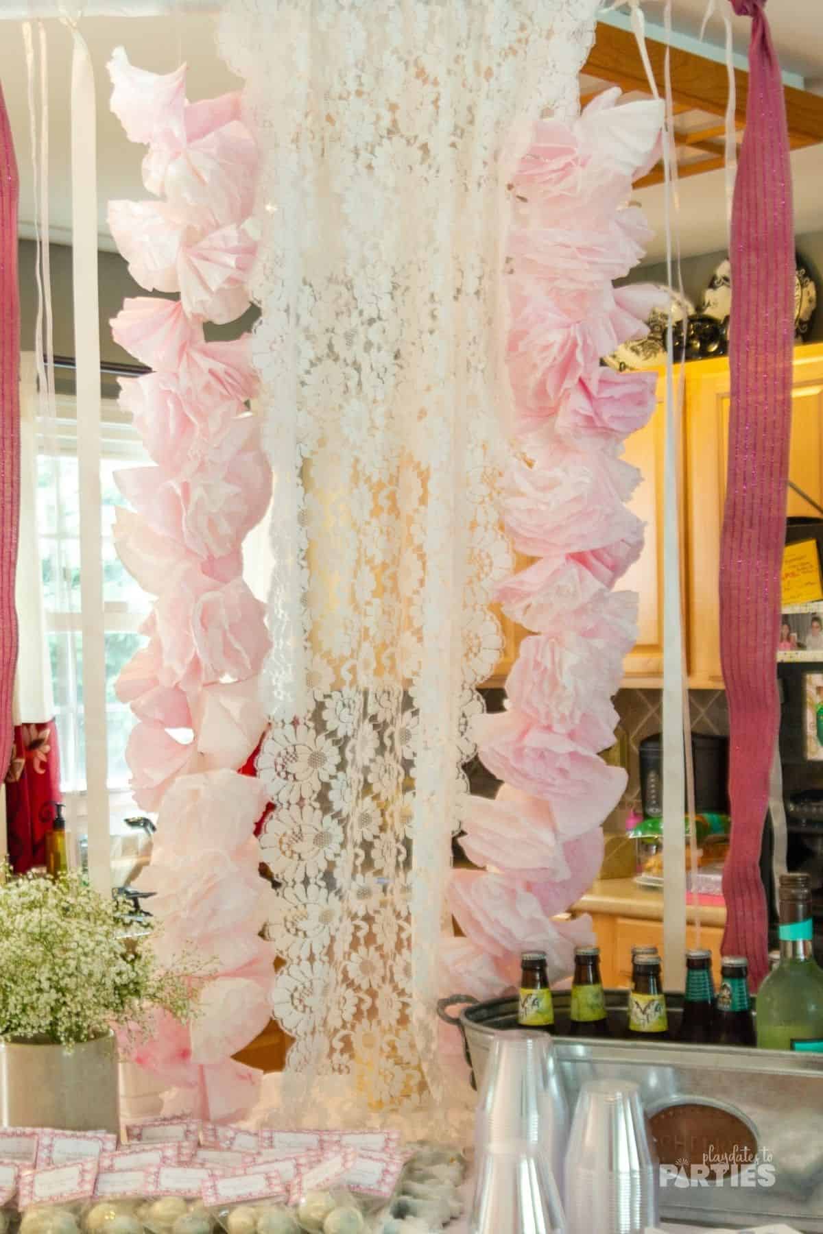 Ping coffee filter garlands, pink lace, and ribbons hanging over a dessert table for a baptism.