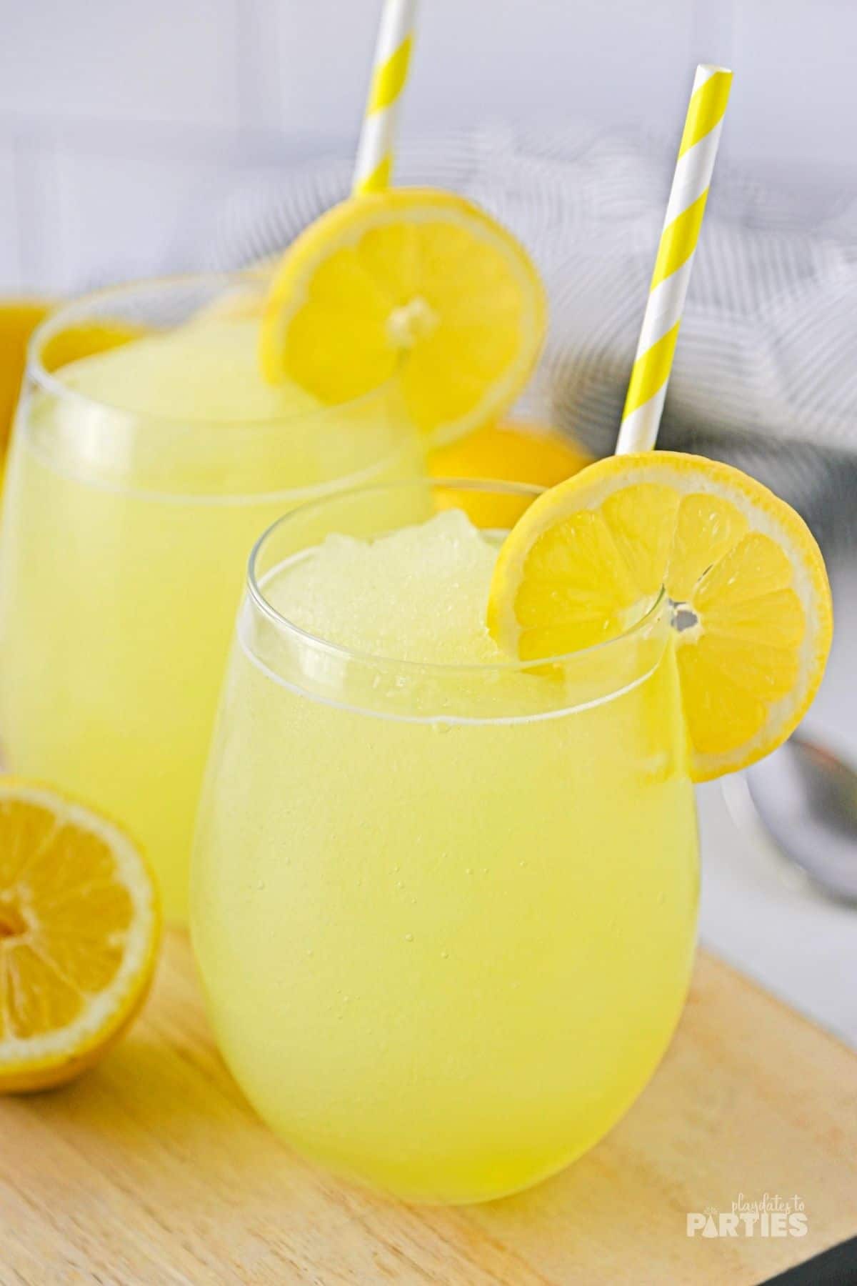 Two glasses filled with frozen lemonade and garnished with lemon slices and paper straws.