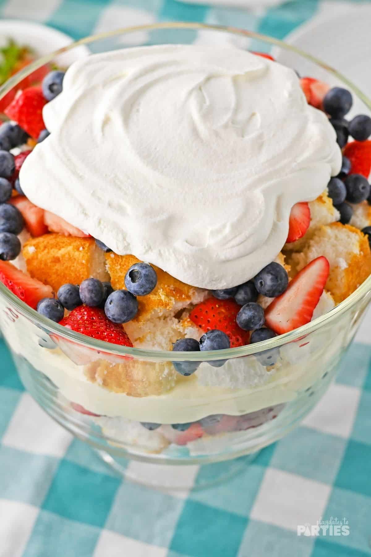 A large pile of whipped cream sits on top of layers of berries, cheesecake pudding mix, and angel food cake.