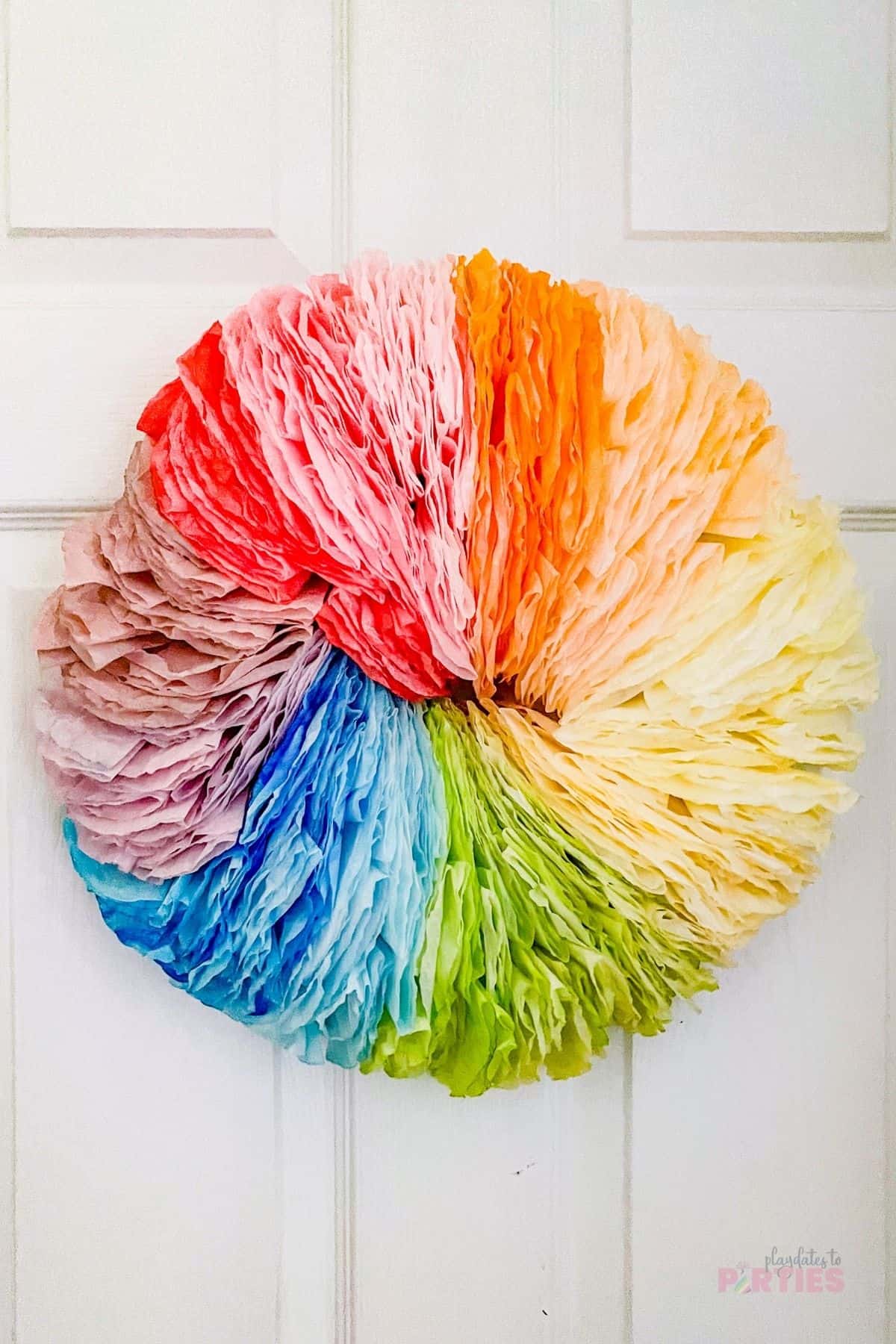 A fluffy rainbow wreath made from coffee filters hangs on an interior door.