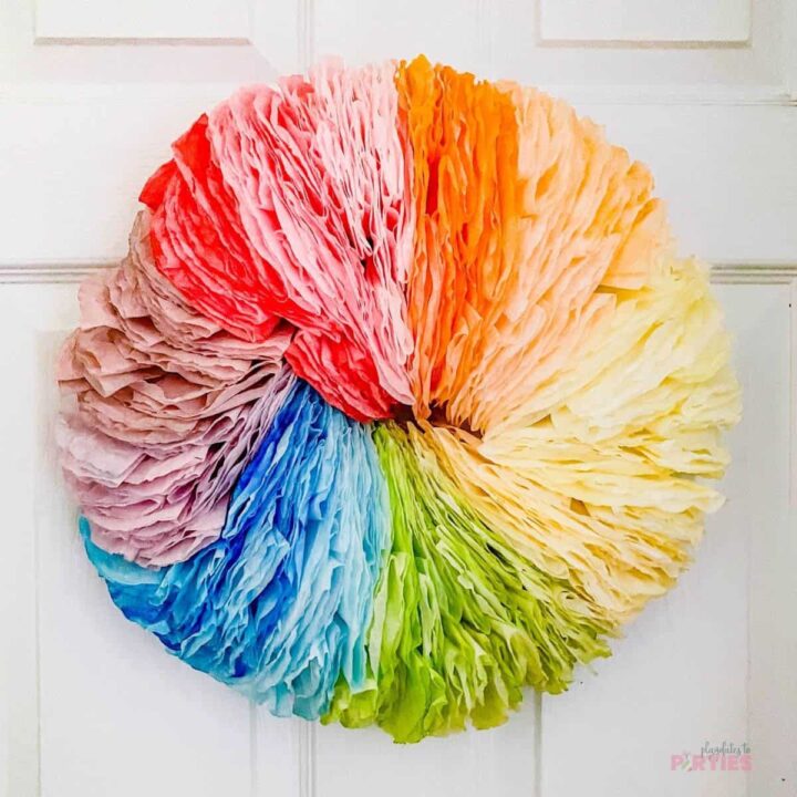 A fluffy DIY rainbow wreath made from coffee filters hangs on an interior door.
