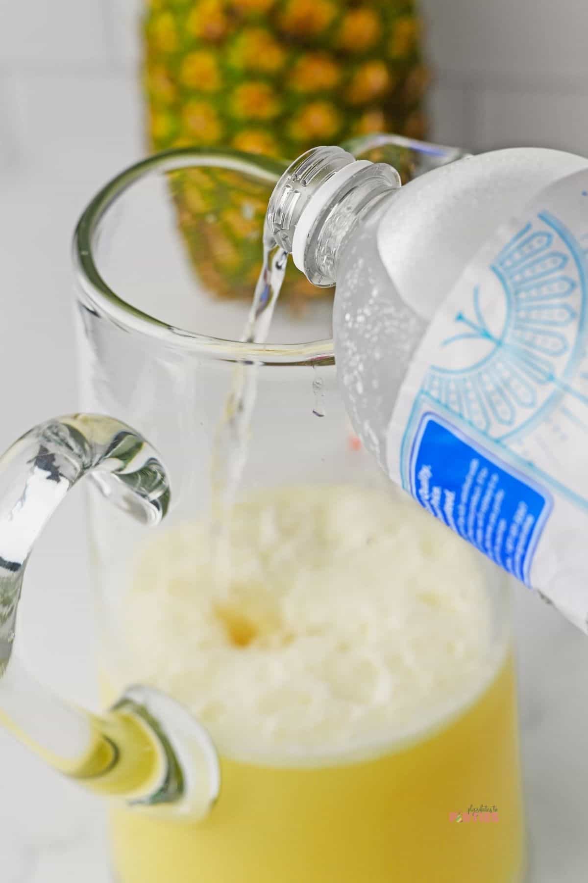 Pouring seltzer water into a pitcher of pineapple juice.