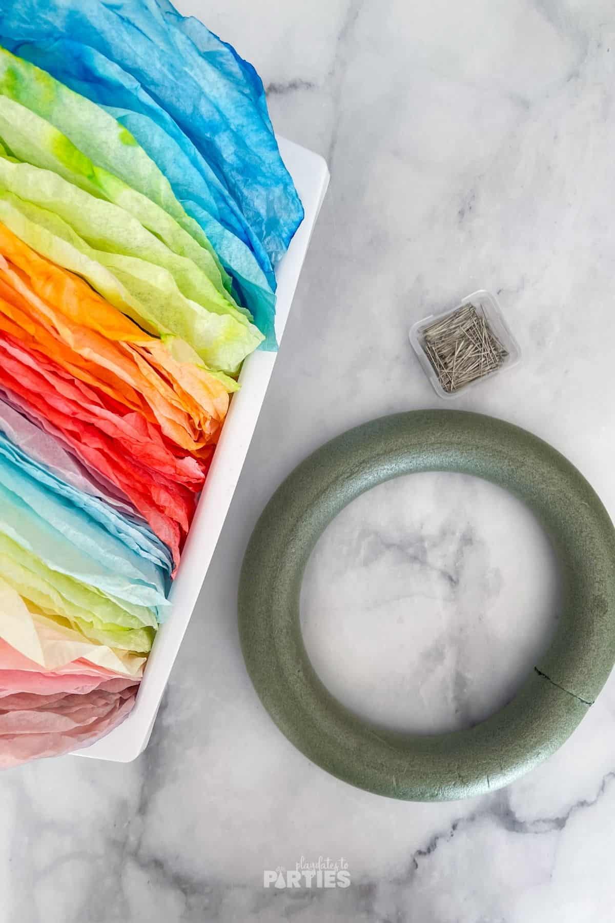 Rainbow dyed coffee filters, foam wreath form, and straight pins on a marble surface.