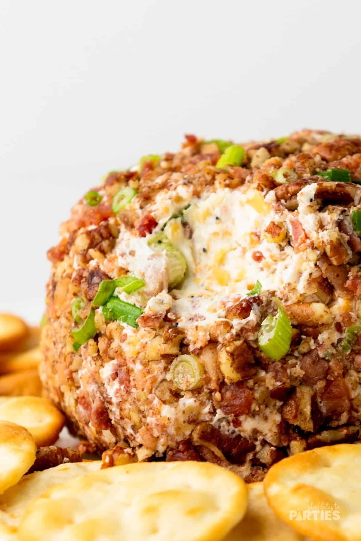A cheeseball appetizer with a bit taken out of it is surrounded by crackers.