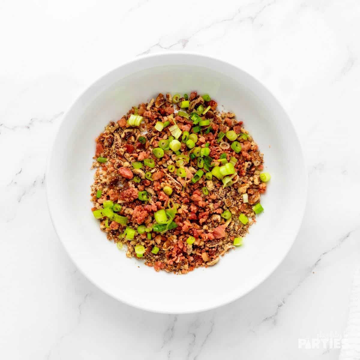 Chopped bacon, green onions, and pecan pieces in a shallow bowl.