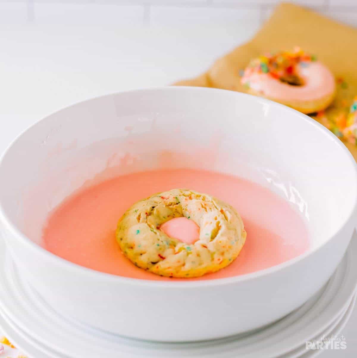 Dipping baked donuts in the strawberry glaze.