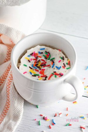 A white mug filled with a single serving mug cake topped with frosting and sprinkles.
